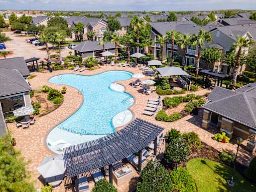 A large swimming pool surrounded by a shaded area and lounge chairs at Avenues at Shadow Creek Ranch Apartments, Pearland, Texas