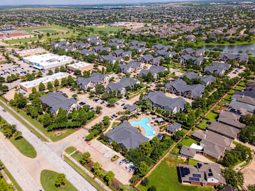A bird's eye view of a residential neighborhood with houses, a swimming pool, and a school at Avenues at Shadow Creek Ranch Apartments, Pearland, Texas