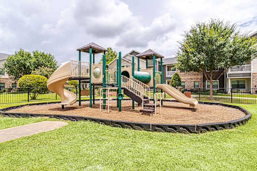 A playground with a green slide and a brown and green play structure at Avenues at Shadow Creek Ranch Apartments, Pearland, TX