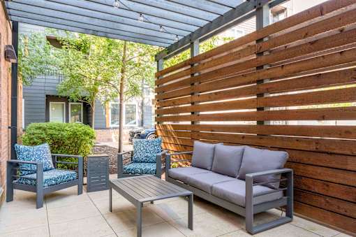 A patio with a grey couch, two chairs and a table.