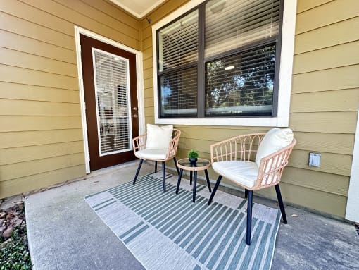 a front porch of a home with two chairs and a table at Grand Villas Apartments, Katy