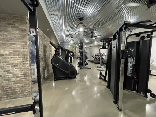 a gym with cardio machines and a brick wall