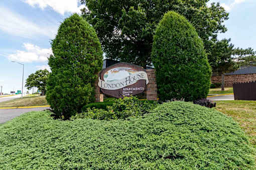 Property entrance sign with mature trees and landscaping at London House Apartments, Lenexa, KS
