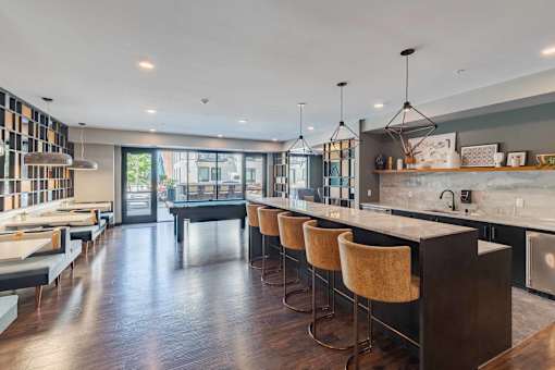 A modern kitchen with a long bar and chairs.