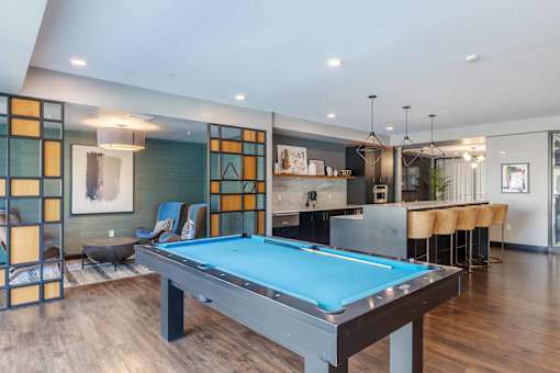 A pool table is in the middle of a room with a bar and a kitchen in the background.
