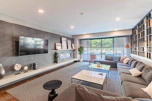 A modern living room with a grey couch, a black coffee table, and a flat screen TV mounted on the wall.