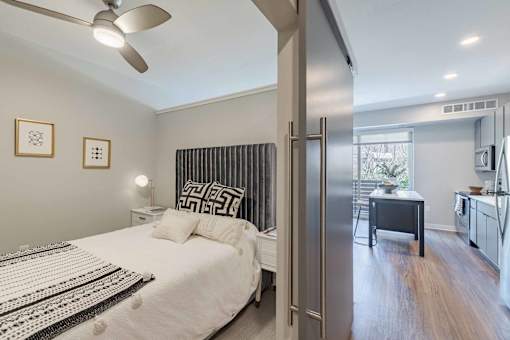 A bedroom with a bed, a ceiling fan, and a door leading to a kitchen.