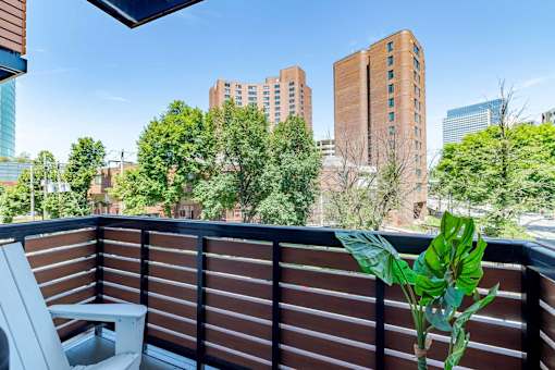 A balcony with a chair and a potted plant overlooking a cityscape.