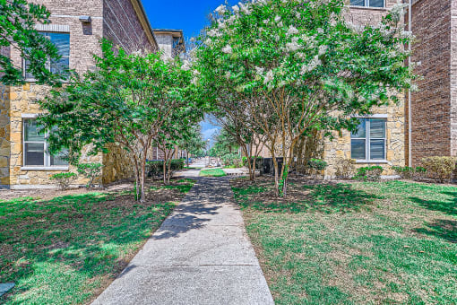 a walkway between two brick buildings with trees at Discovery at Craig Ranch, McKinney, 75070