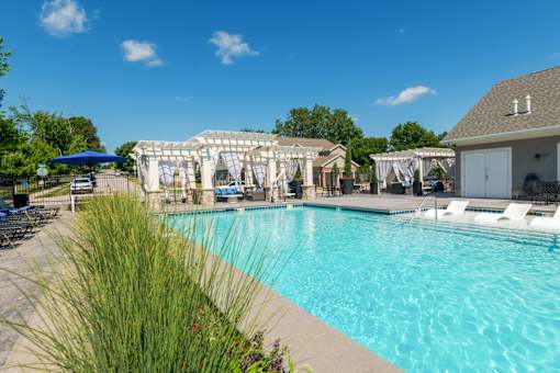 A large swimming pool with a blue umbrella and lounge chairs.