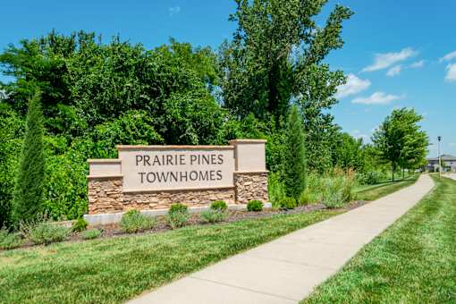 A sign for Prairie Pines Townhomes stands in front of a green lawn.