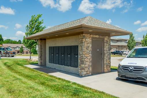 A stone and concrete building with a brown roof and a van parked in front.