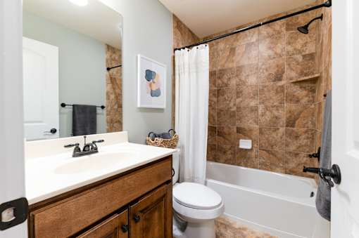 A bathroom with a brown tiled shower area and a white toilet.