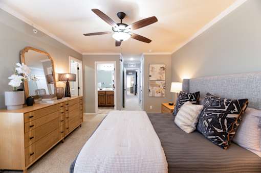 A bedroom with a bed, dresser, mirror, and ceiling fan.