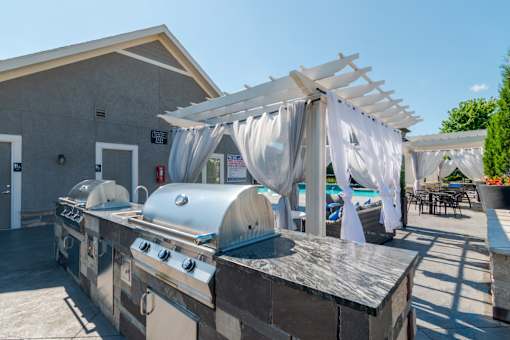 A barbecue grill is set up on a patio with a pool in the background.