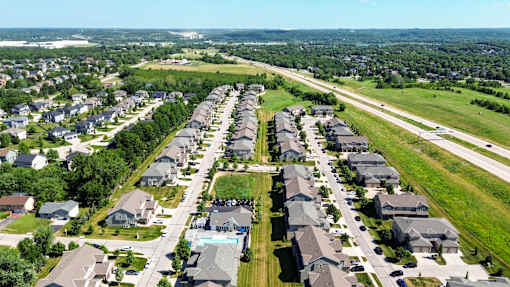 A bird's eye view of a residential area with rows of houses and a swimming pool in the middle.