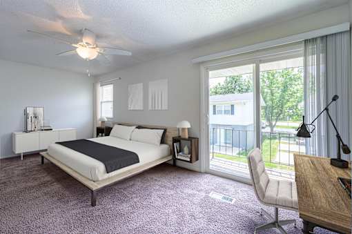 A bedroom with a large bed and a balcony view at Spring Creek Townhomes Apartments, Springfield, IL