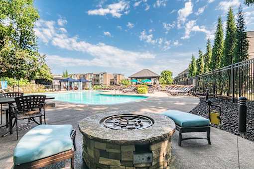 A pool area with a fountain in the middle and chairs around it.