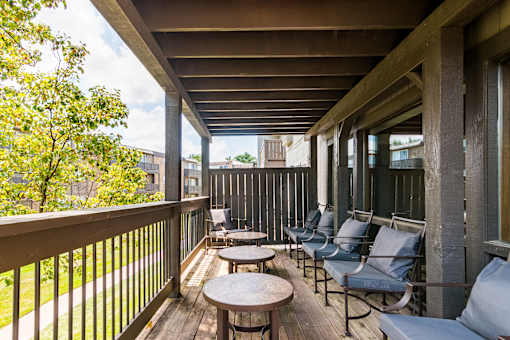 A wooden balcony with chairs and tables.