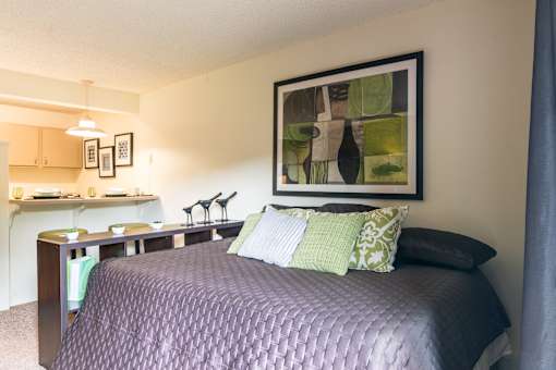 A bedroom with a bed, a desk, and a painting on the wall.