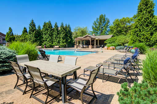 A poolside table and chairs are set up in front of a pool and a gazebo at Sovereign at Overland Park Apartments, Kansas, 66213