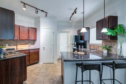 A kitchen with dark wood cabinets and a black counter top at Sovereign at Overland Park Apartments, Overland Park Kansas
