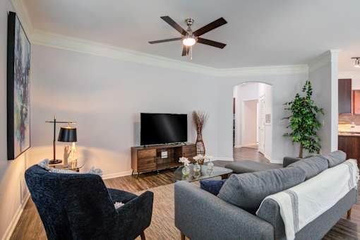 A living room with a grey couch, a blue chair, a television, and a ceiling fan at Sovereign at Overland Park Apartments, Overland Park, KS
