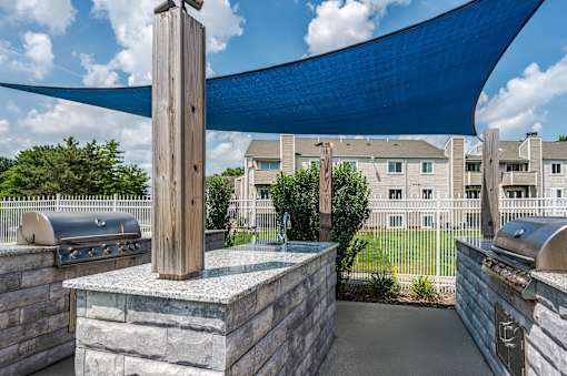 A patio with a grill and a blue shade sail.