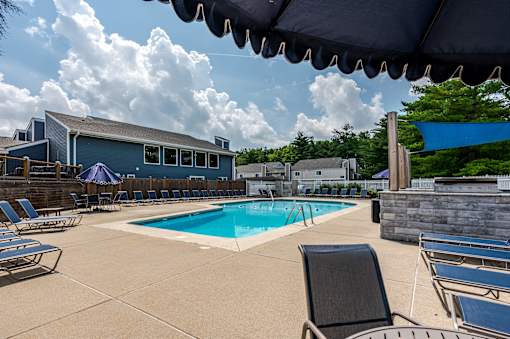 A pool surrounded by lounge chairs and umbrellas with a house in the background.