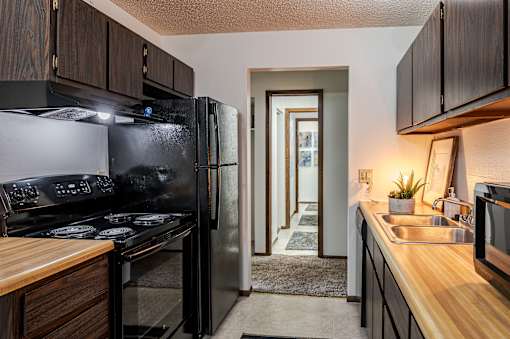 A kitchen with a black refrigerator and wooden countertops.