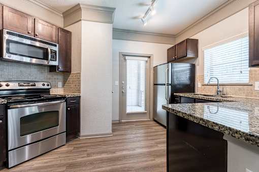 A kitchen with dark brown cabinets and stainless steel appliances at Waterstone at Cinco Ranch Apartments, Texas, 77450