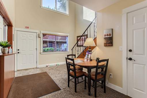 A dining room with a brown rug and a wooden table with chairs.