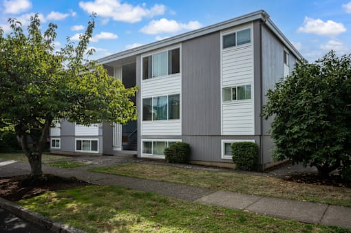 A grey building with white trim and windows is surrounded by greenery.