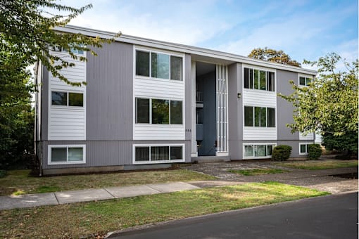 A grey and white building with a tree in front.