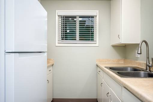 A kitchen with a white refrigerator and a window with blinds.