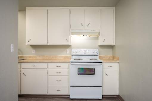 A white stove in a kitchen with white cabinets.