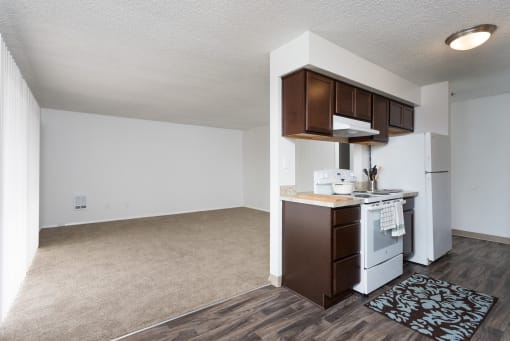 an empty living room and kitchen with white appliances and wood flooring