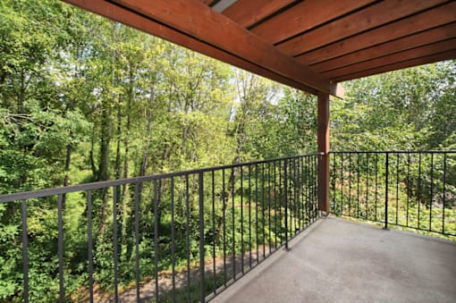 A balcony with a metal railing and a view of a wooded area.