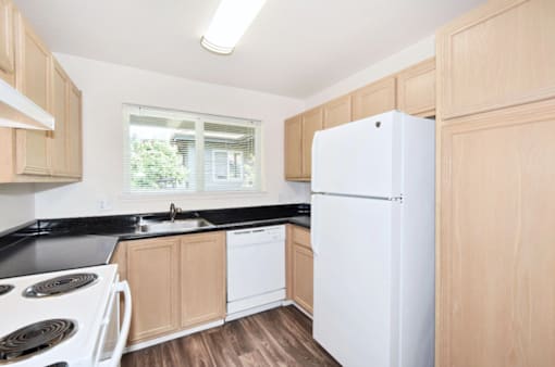 A kitchen with a white refrigerator, black countertops, and wooden cabinets.