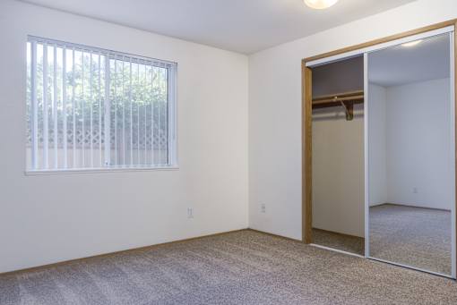 an empty bedroom with a large window and a mirrored closet
