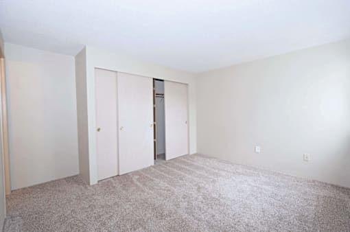 A room with carpeted floor and white walls with a doorway leading to another room.