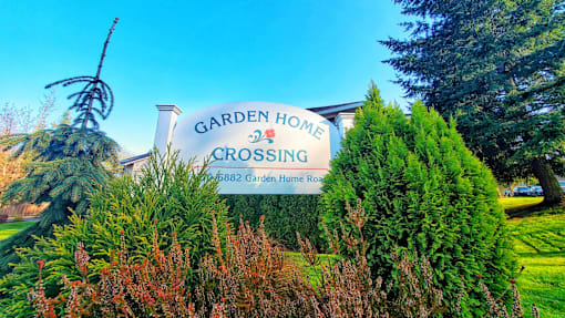 A sign for Garden Home Crossing stands in front of a green hedge.