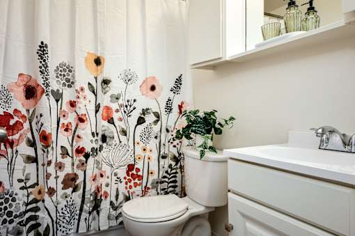 A white toilet sits next to a sink in a bathroom with a floral shower curtain.