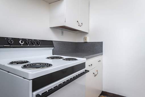 A white stove with a black top is in a kitchen with white cabinets.