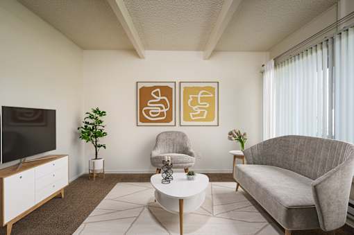 A living room with a grey couch, a white coffee table, a television, and two framed artworks on the wall.