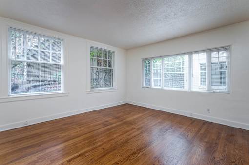 A room with wooden floors and three windows.
