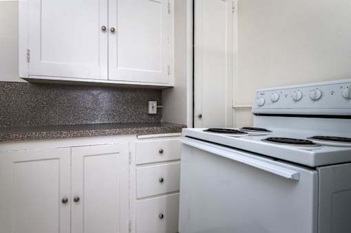 A white stove sits in a kitchen with white cabinets.