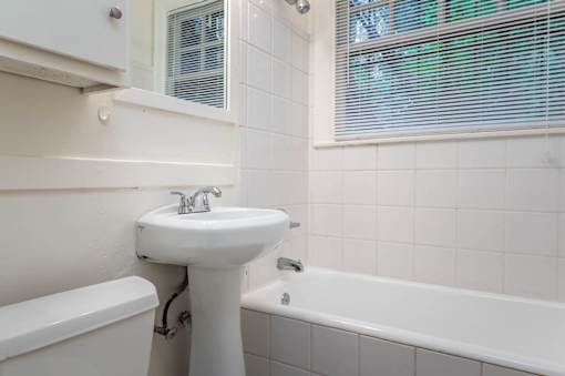 A white sink is in a white bathroom with a white tub.