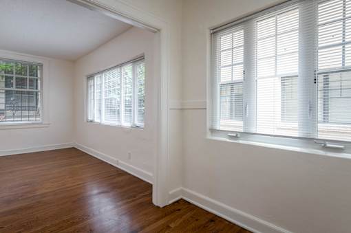 A room with wooden floors and two windows with blinds.