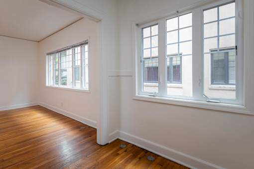 A room with wooden floors and three windows.
